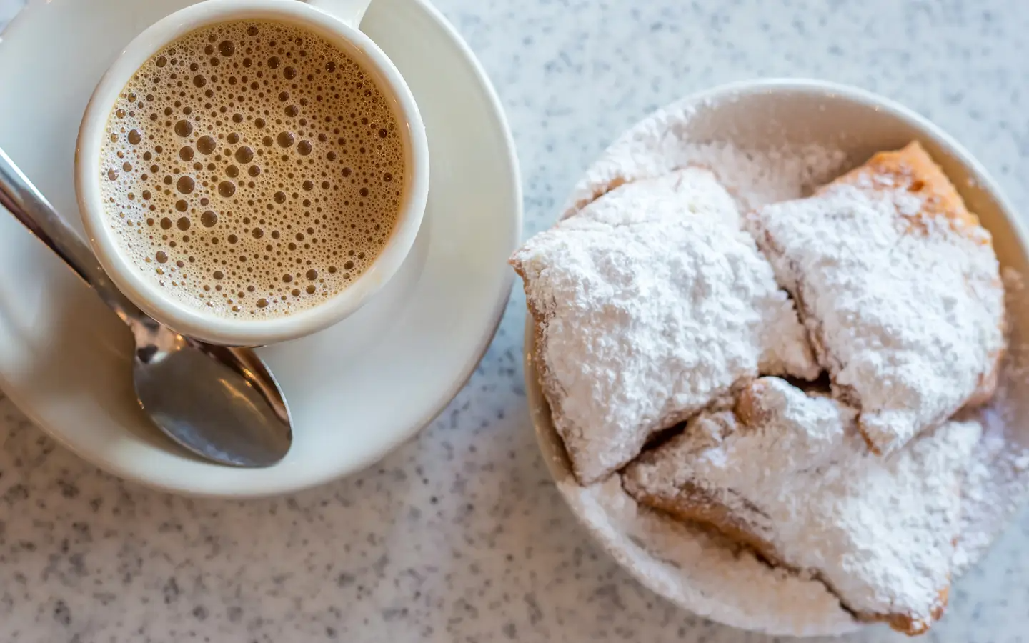 A table with a plate of beignets and a cup of coffee